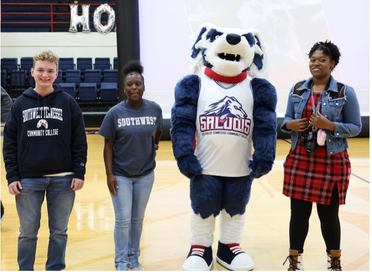 Suki the saluqi mascot a Dog costume with a saluqis jersey and 3 people stand on the basketball court