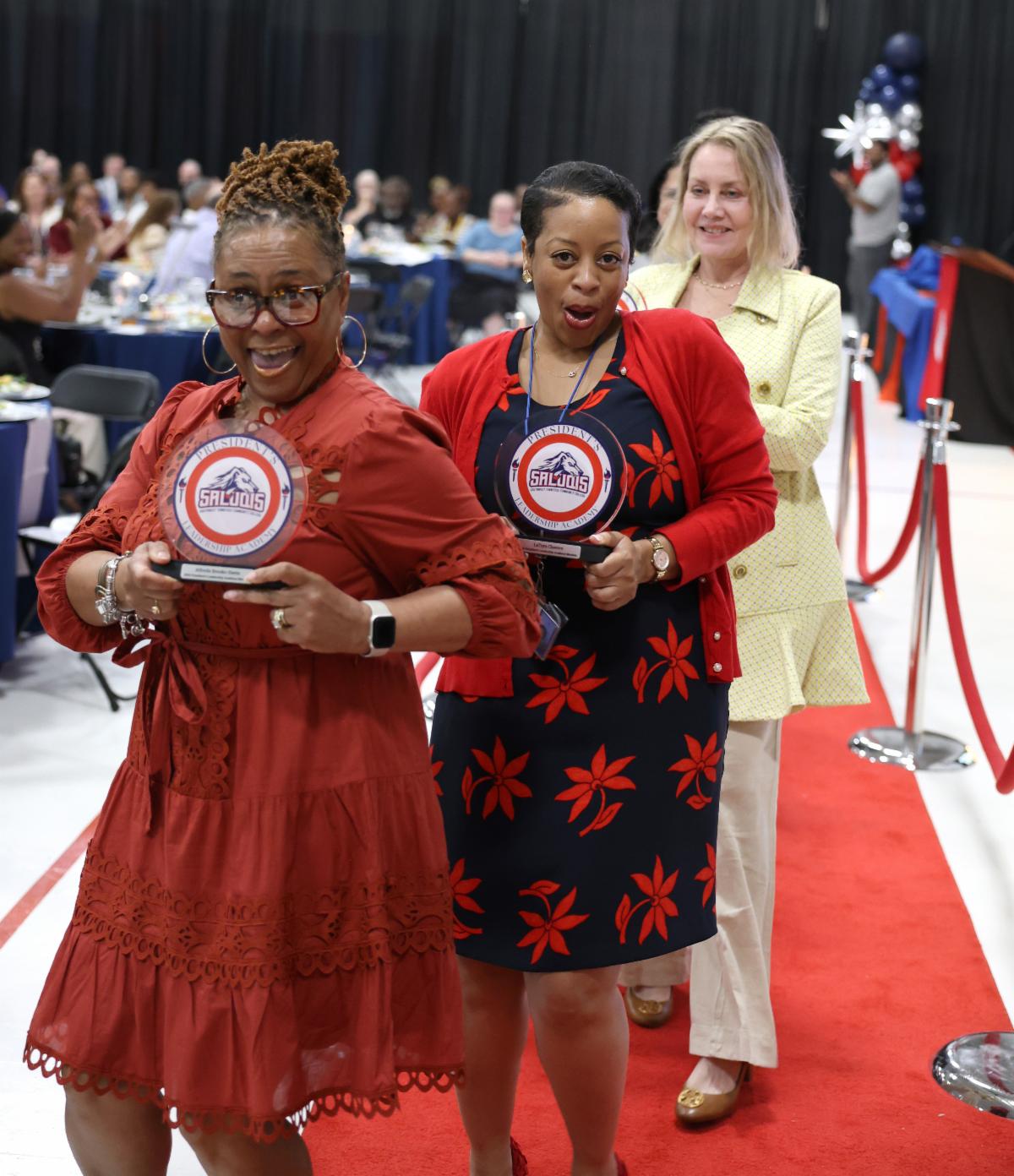 2 women walking down red carpet with awards